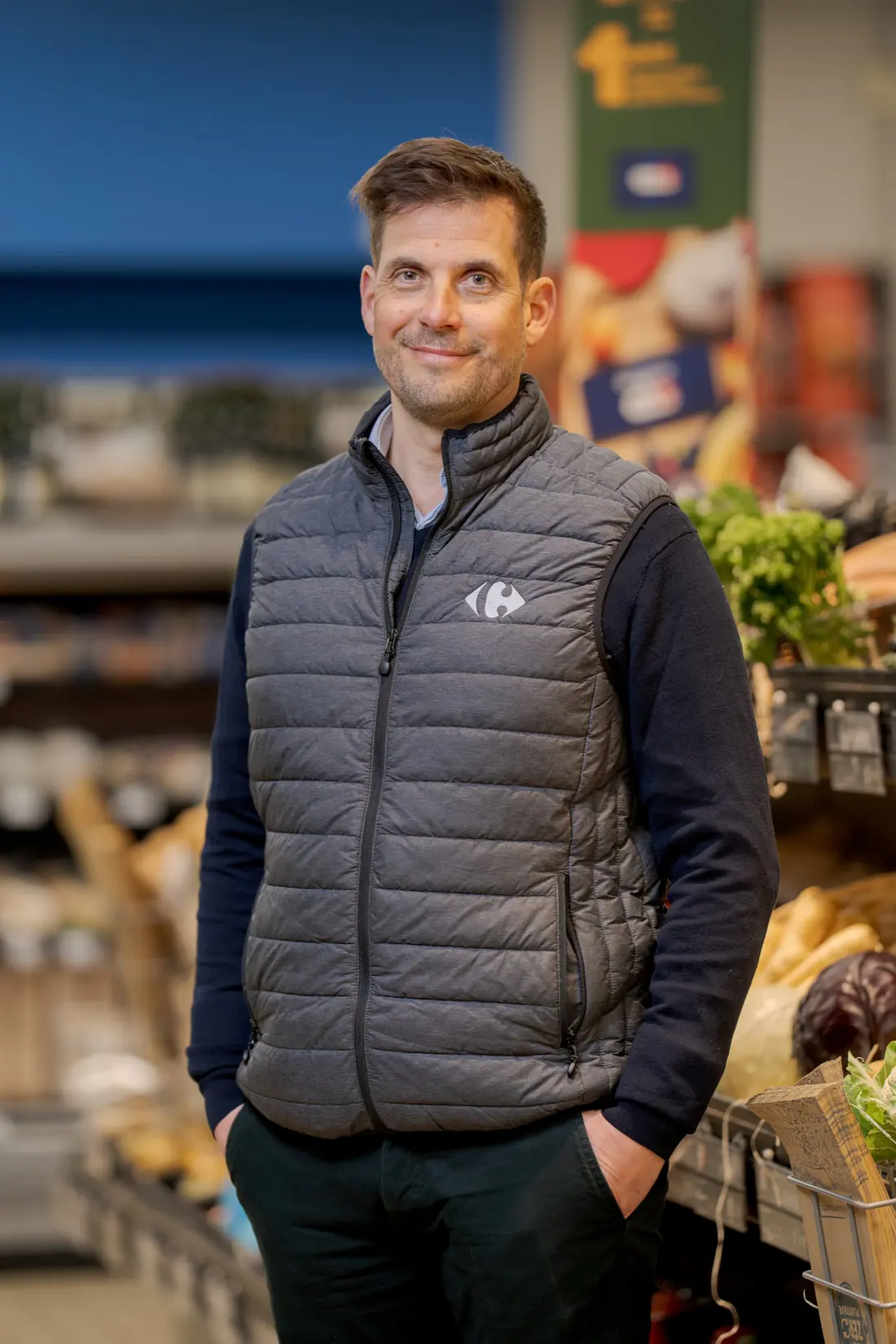Portrait d'un franchisé Carrefour Proximité dans son magasin, veste aux couleurs de l'enseigne
